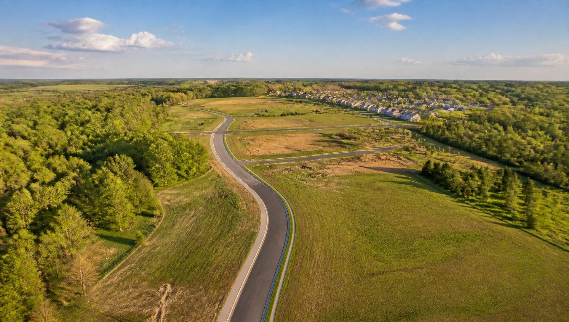 Bright aerial view of open land, a new road, and a residential neighborhood
